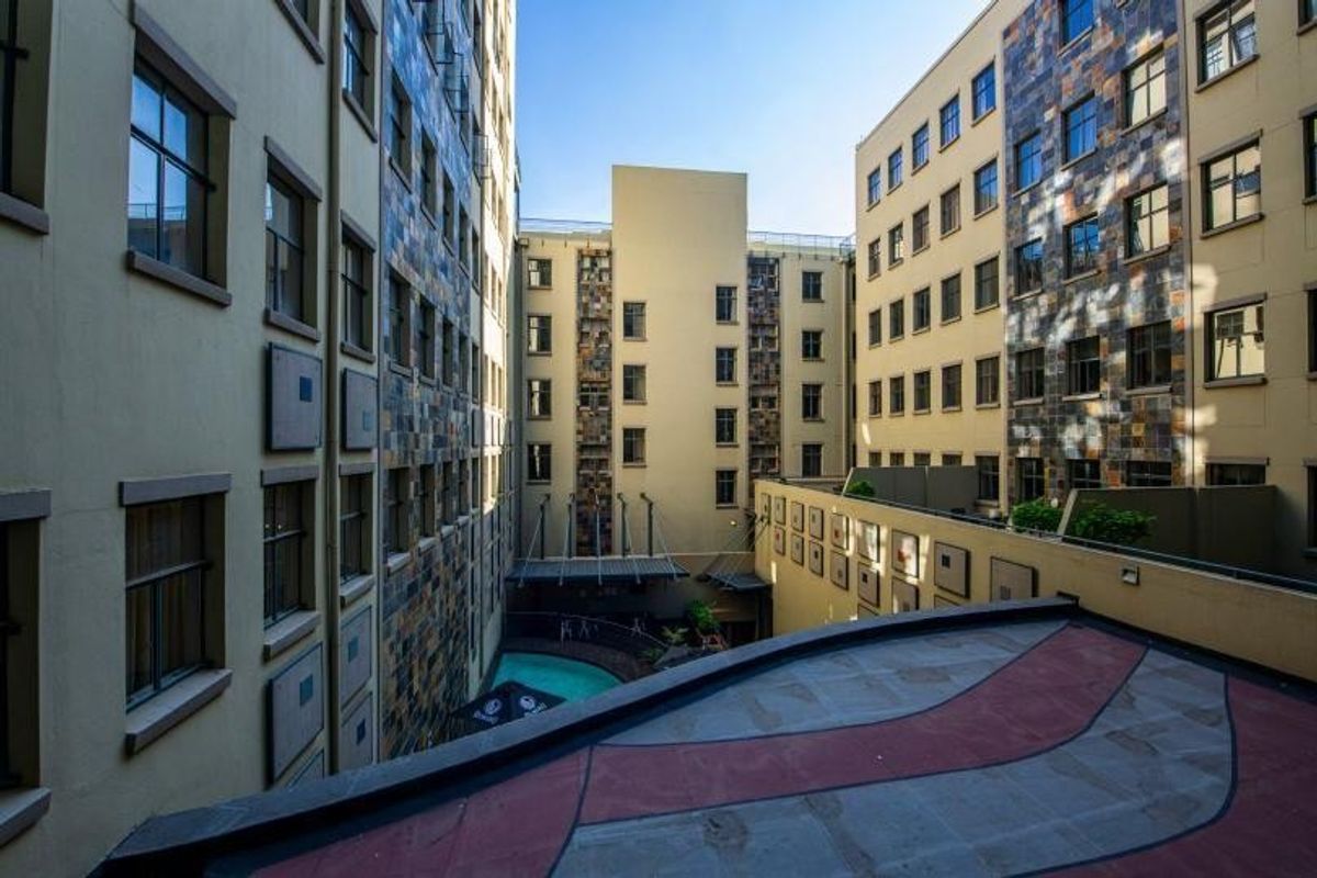 An elevated view of an apartment complex courtyard featuring stone-clad facades, a swimming pool, and a paved balcony area.