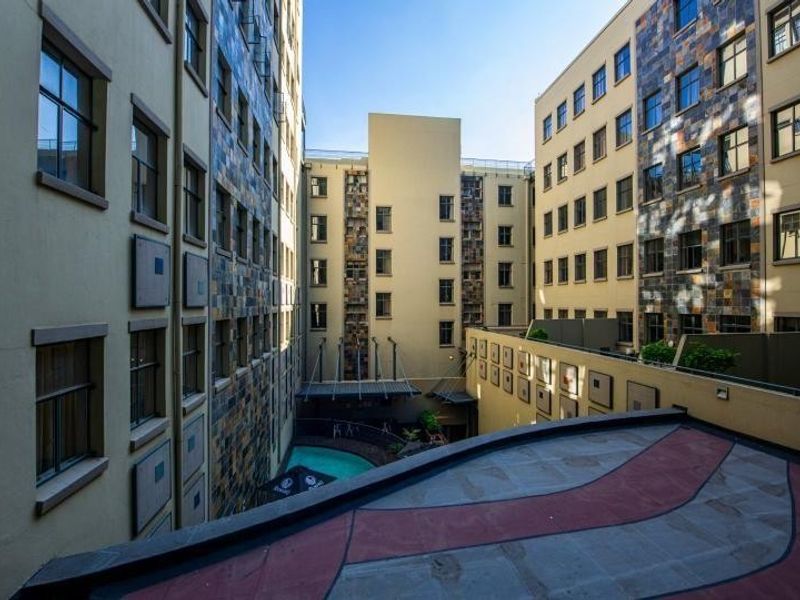 An elevated view of an apartment complex courtyard featuring stone-clad facades, a swimming pool, and a paved balcony area.
