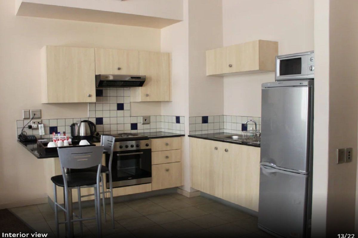 Compact kitchen featuring light wood-finish cabinetry, tiled backsplash, built-in oven and hob, and tiled flooring.