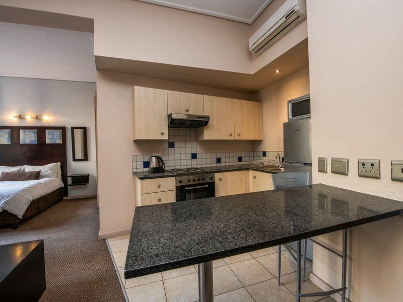 Open-plan studio apartment featuring a compact kitchen with granite countertops and built-in cabinetry, seamlessly flowing into the carpeted bedroom area.