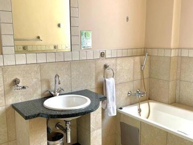 A functional bathroom featuring a built-in vanity with an undermount sink, a wall-mounted mirror, and a bathtub with a handheld shower attachment.