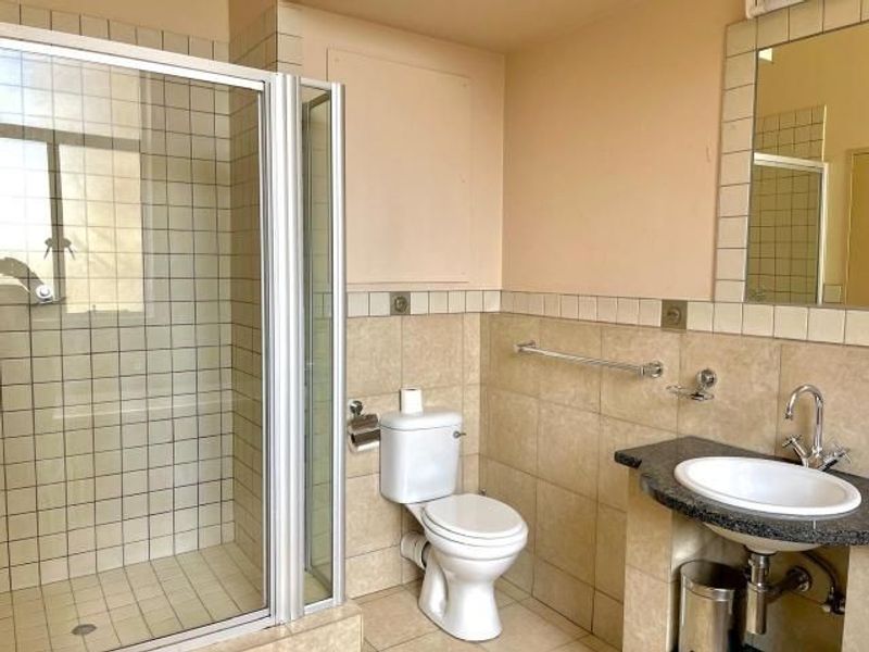 A functional bathroom featuring a glass-enclosed shower, a standard toilet, and a vanity basin with a granite countertop and wall-mounted mirror.