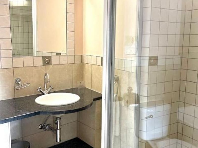A clean, functional bathroom featuring a granite-topped vanity, wall-mounted mirror, glass shower enclosure, and standard toilet with neutral ceramic tiling.
