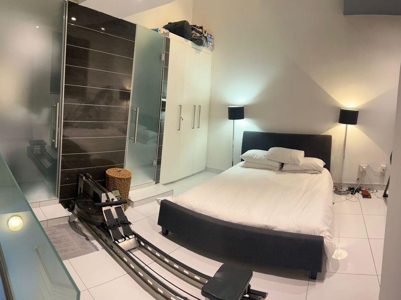A modern bedroom featuring tiled flooring, a built-in wardrobe, and a glass-enclosed en-suite bathroom area.