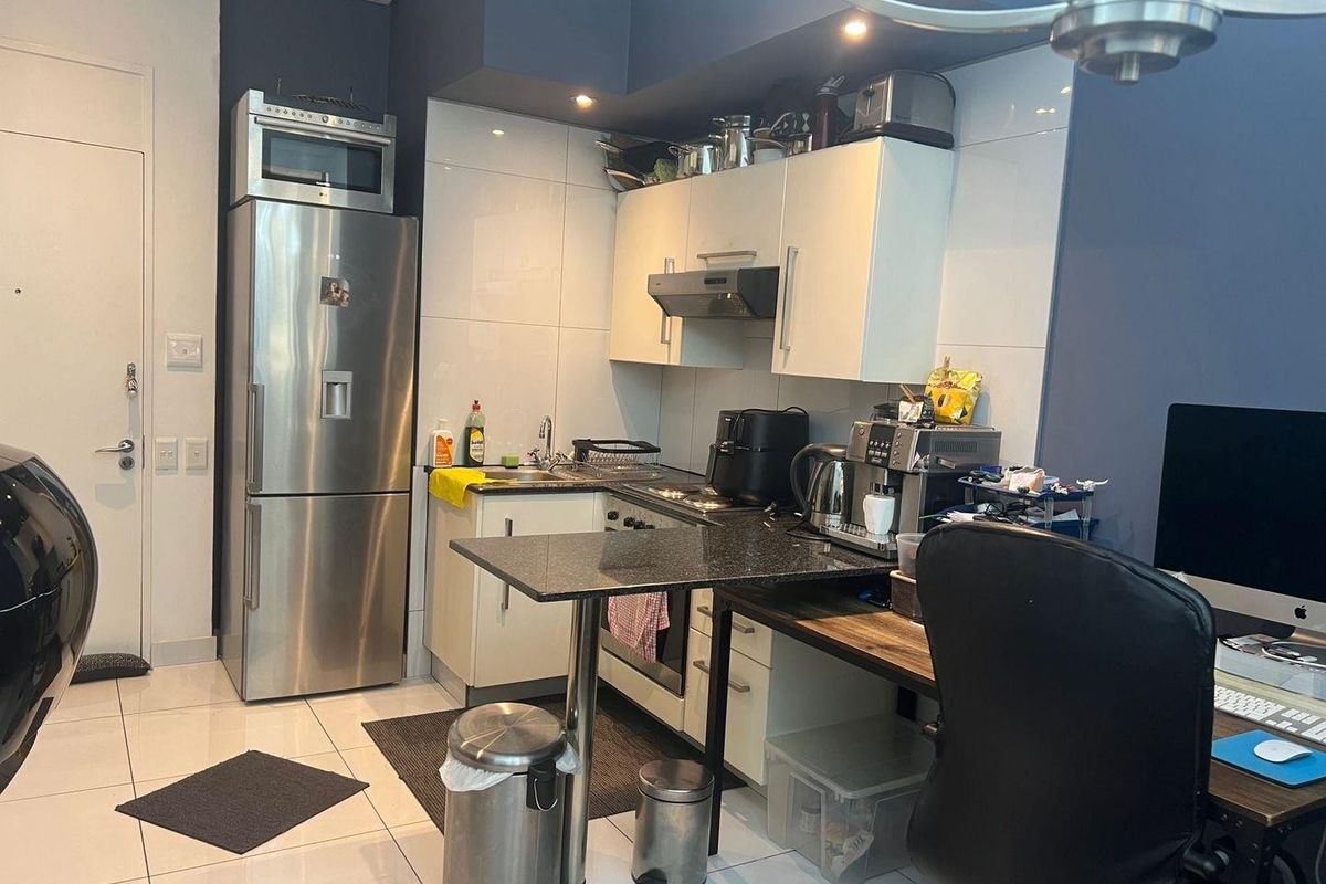 Compact kitchen featuring white cabinetry, stainless steel appliances, a breakfast bar, and tiled flooring, integrated into a multi-functional living space.