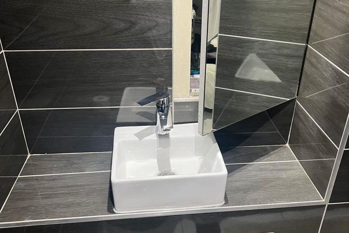 A compact bathroom vanity area featuring a modern square vessel sink, chrome tap, and dark wood-effect tiled splashback with an integrated mirrored cabinet.
