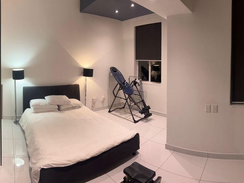 A modern bedroom featuring tiled flooring, recessed ceiling lighting, and a frosted glass door leading to an en-suite bathroom.