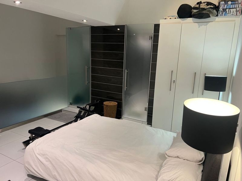 A modern bedroom featuring built-in cupboards, sleek tiled flooring, and frosted glass doors leading to an en-suite bathroom.