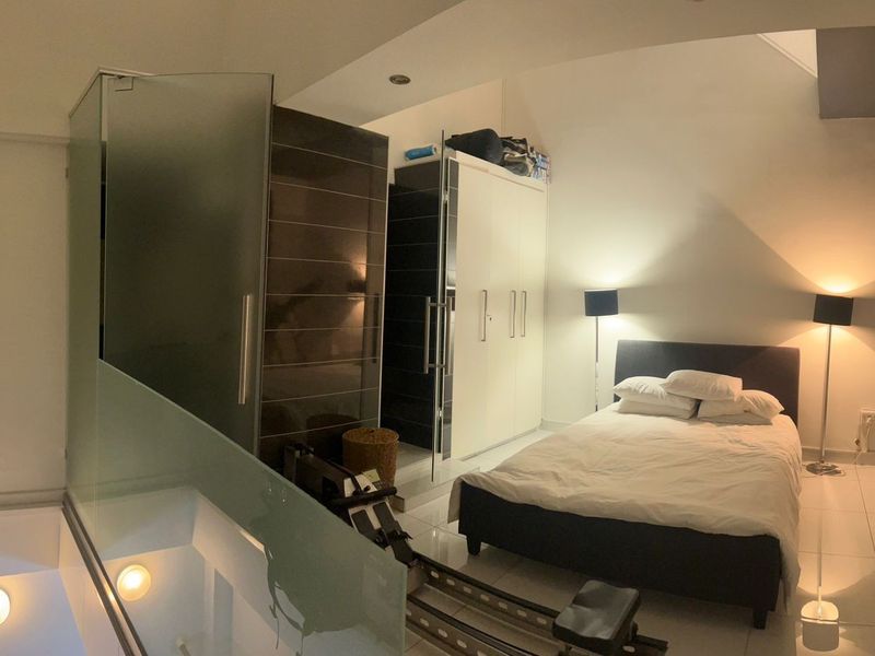 A modern bedroom featuring tiled flooring, built-in wardrobe storage, and a glass partition separating the sleeping area from the rest of the space.