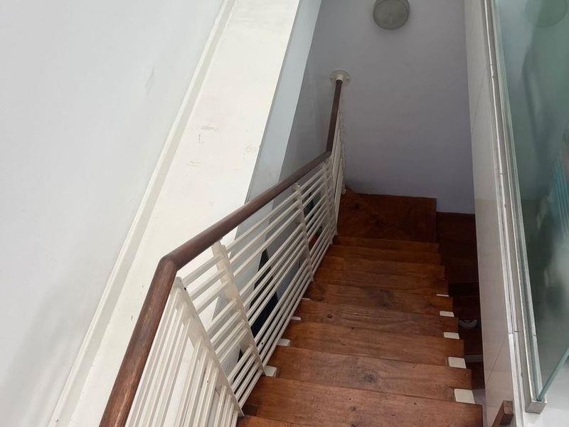 A wooden staircase featuring a white metal balustrade with a timber handrail, leading down to a lower level with a glass partition.