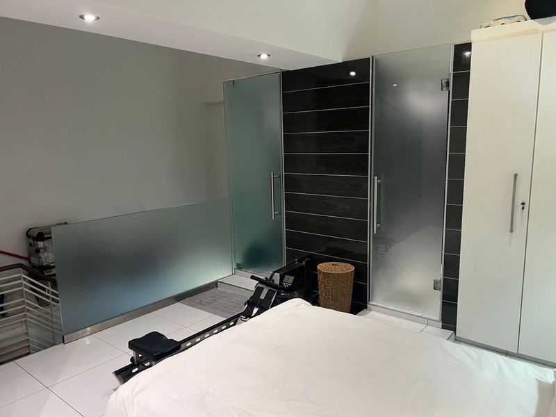 Modern bedroom featuring tiled flooring, recessed lighting, a glass balustrade, and built-in wardrobes with frosted glass doors.