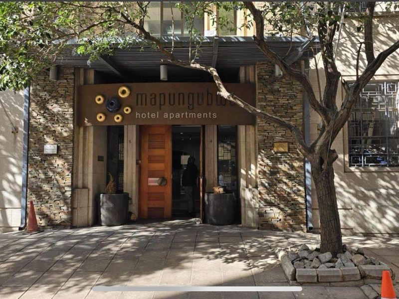 The front entrance of the Mapungubwe Hotel Apartments, featuring stone cladding, a metal awning, and a prominent timber door.