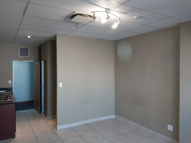 Open plan living area featuring tiled floors, track lighting, and a partially open kitchen, currently vacant and in need of minor ceiling repairs.