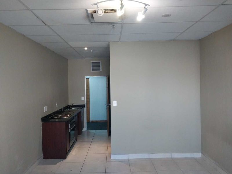 A compact, empty kitchen area featuring dark cabinetry, granite countertops, built-in oven and hob, with tiled flooring and a drop ceiling.
