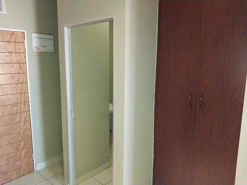 A functional hallway area featuring tiled flooring and a built-in wooden cupboard, providing access to adjacent rooms.
