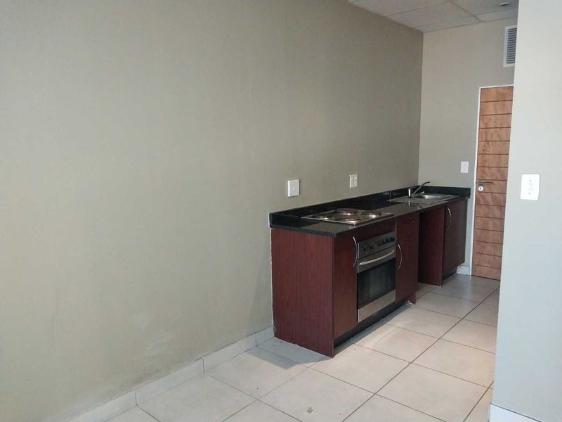 A compact, empty kitchen featuring dark wood cabinetry, granite countertops, a built-in oven, electric hob, and a stainless steel sink with tiled flooring.