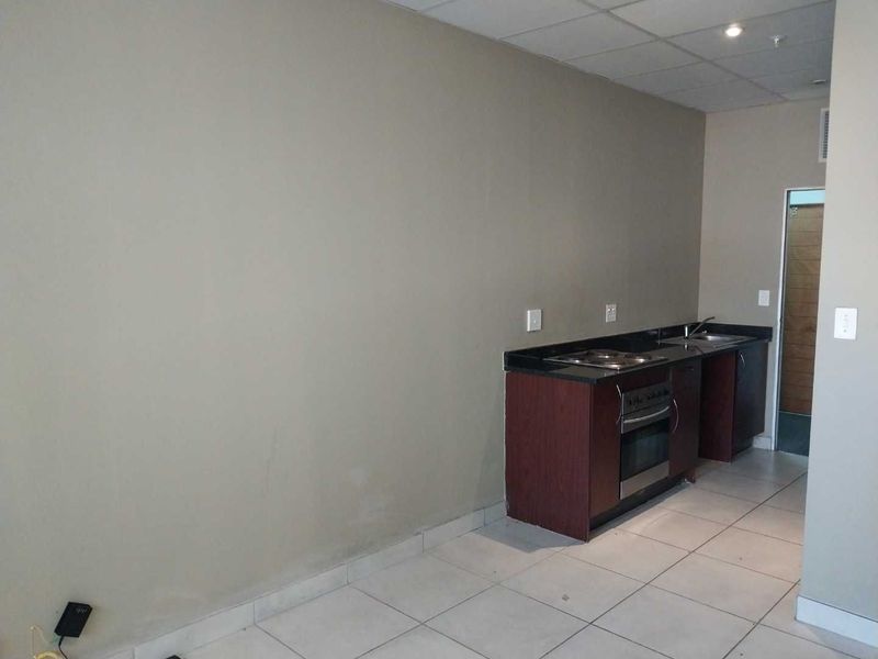 A compact, empty kitchen area featuring dark wood cabinetry, granite countertops, a built-in oven, and tiled flooring.