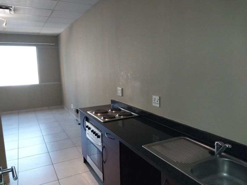A functional kitchen area featuring a built-in oven, electric hob, granite countertops, and a stainless steel sink, set within an open-plan living space.