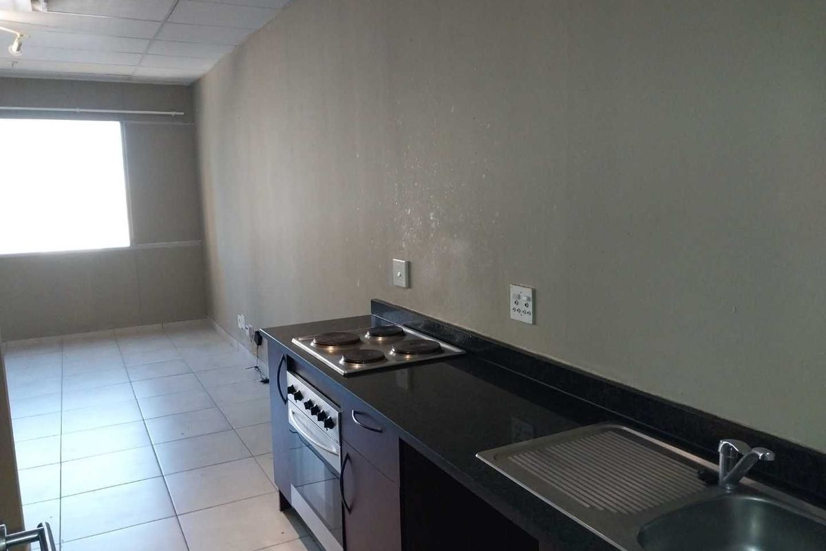 A functional kitchen area featuring a built-in oven, electric hob, granite countertops, and a stainless steel sink, set within an open-plan living space.