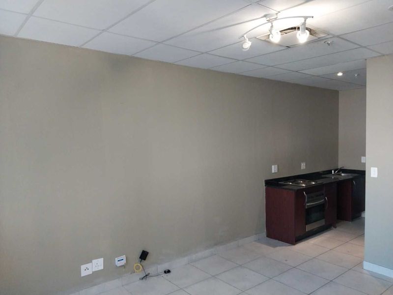 An open-plan living and kitchen area featuring tiled flooring, a drop ceiling, and a compact kitchenette with built-in oven and hob.