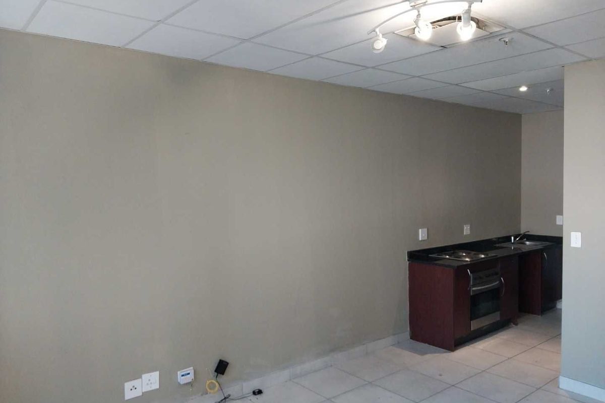 An open-plan living and kitchen area featuring tiled flooring, a drop ceiling, and a compact kitchenette with built-in oven and hob.