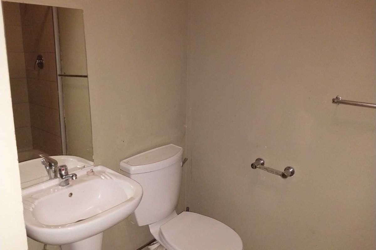 A functional bathroom featuring a pedestal basin, toilet, and shower enclosure, requiring cosmetic updates to improve its overall appearance.