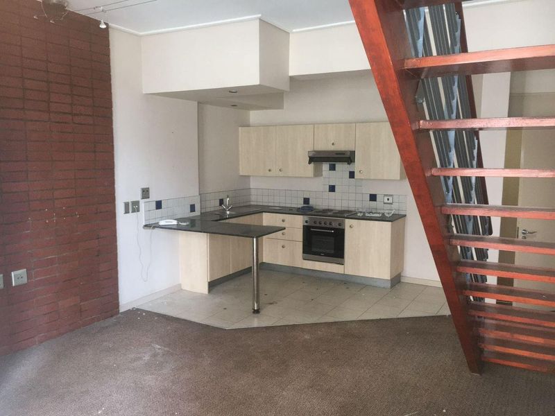 Open-plan kitchen area featuring built-in cabinetry, integrated appliances, and an exposed brick wall, adjacent to an open-tread staircase in an apartment setting.