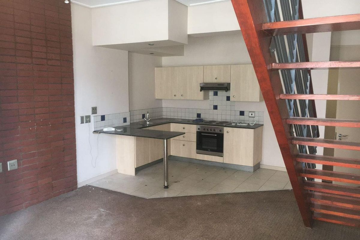 Open-plan kitchen area featuring built-in cabinetry, integrated appliances, and an exposed brick wall, adjacent to an open-tread staircase in an apartment setting.