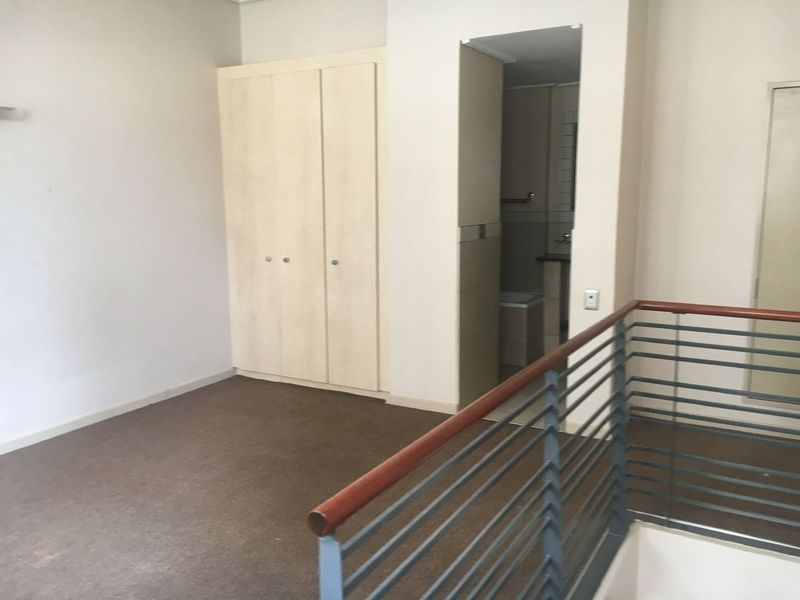 An empty bedroom featuring built-in wardrobes, carpet flooring, and a metal balustrade overlooking the lower level, with an adjacent bathroom entrance.