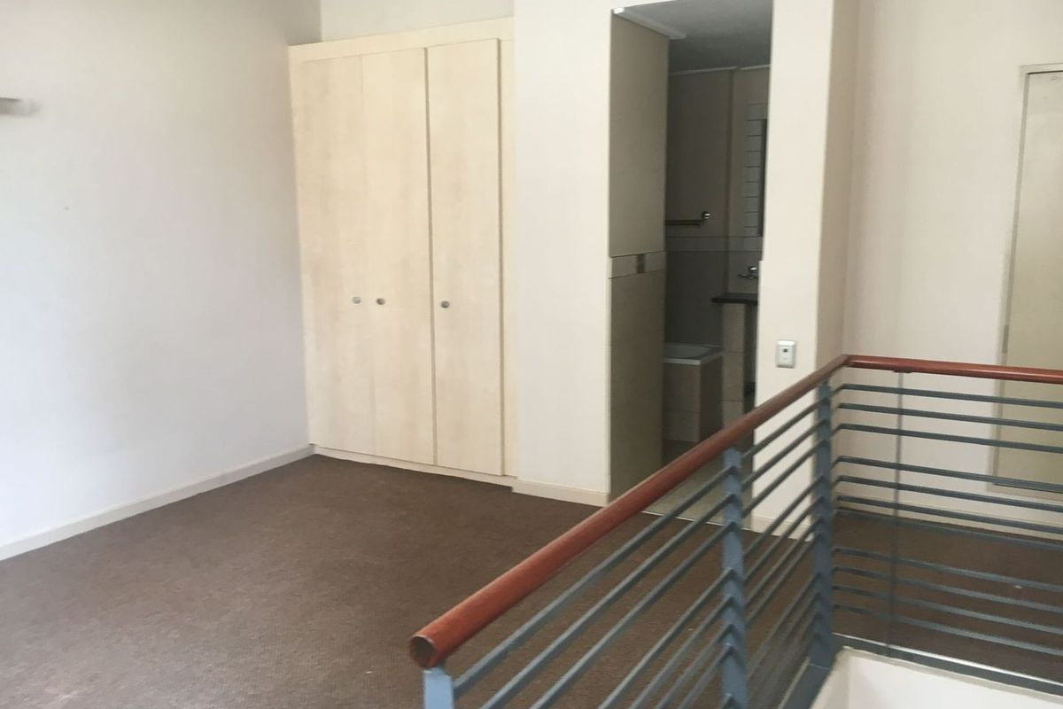 An empty bedroom featuring built-in wardrobes, carpet flooring, and a metal balustrade overlooking the lower level, with an adjacent bathroom entrance.