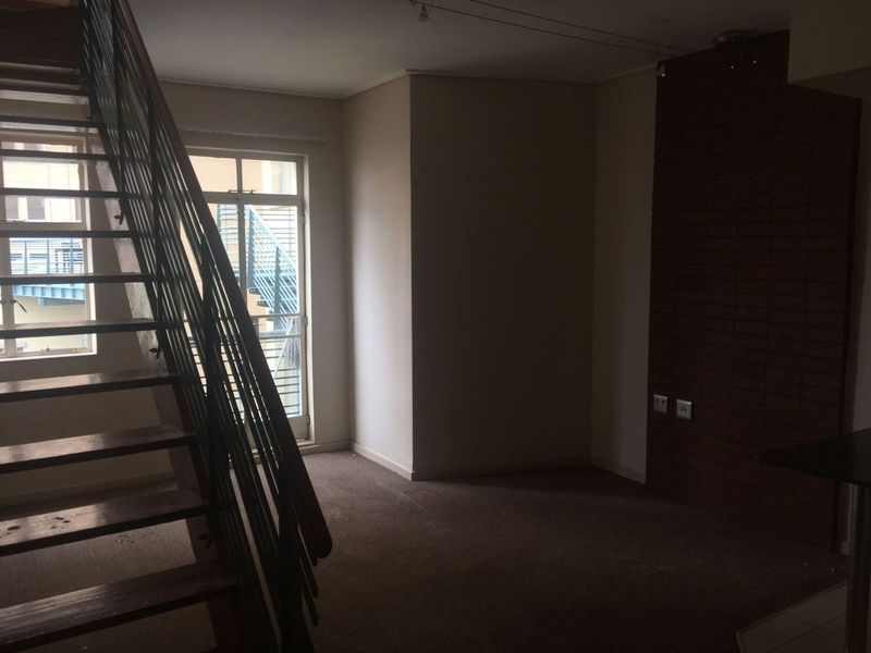 An empty living area featuring an exposed brick wall, carpeted flooring, and an internal staircase leading to the upper level.
