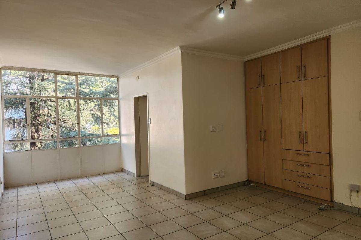 Spacious bedroom featuring neutral tiled flooring, large windows providing natural light, and extensive built-in wooden cabinetry for storage.