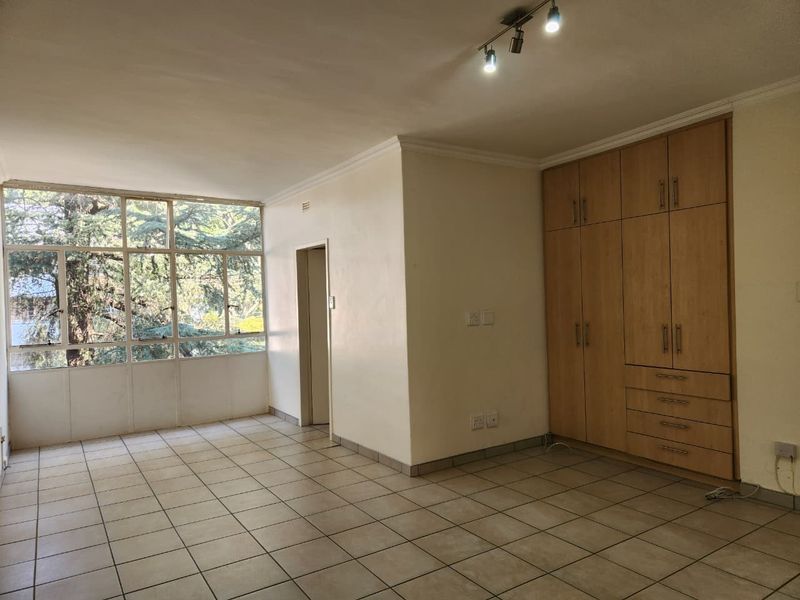 Spacious bedroom featuring neutral tiled flooring, large windows providing natural light, and extensive built-in wooden cabinetry for storage.