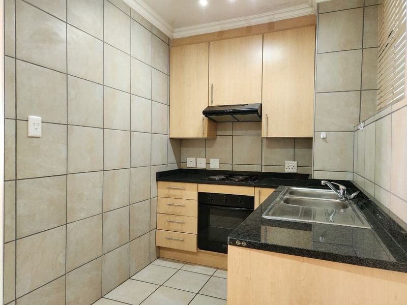A compact kitchen featuring light wood cabinetry, granite countertops, a built-in oven, hob, extractor fan, and full-height wall tiling.