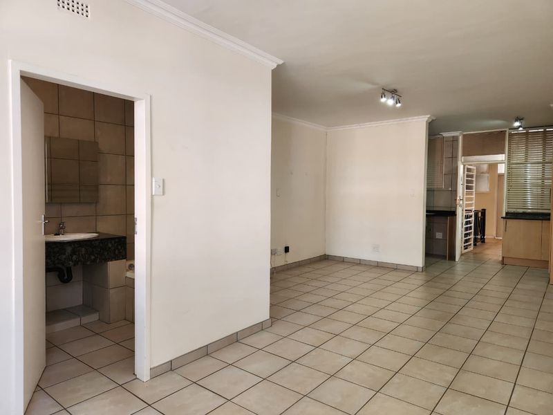 Spacious open-plan living area featuring tiled floors, neutral walls, and an adjacent bathroom and kitchen with granite countertops.