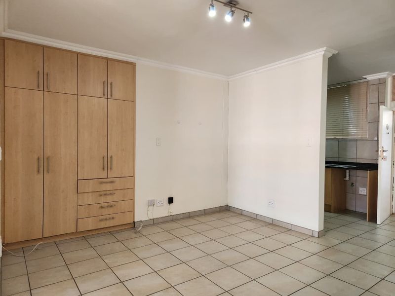 Open plan living area featuring neutral tiled flooring, built-in wooden cupboards, and ceiling-mounted spotlights, with an adjacent view into the kitchen area.