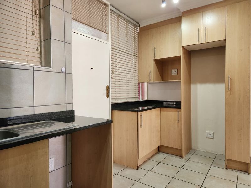 A functional kitchen featuring light wood laminate cabinetry, dark granite countertops, ceramic floor tiling, and integrated sink area with natural light from window blinds.