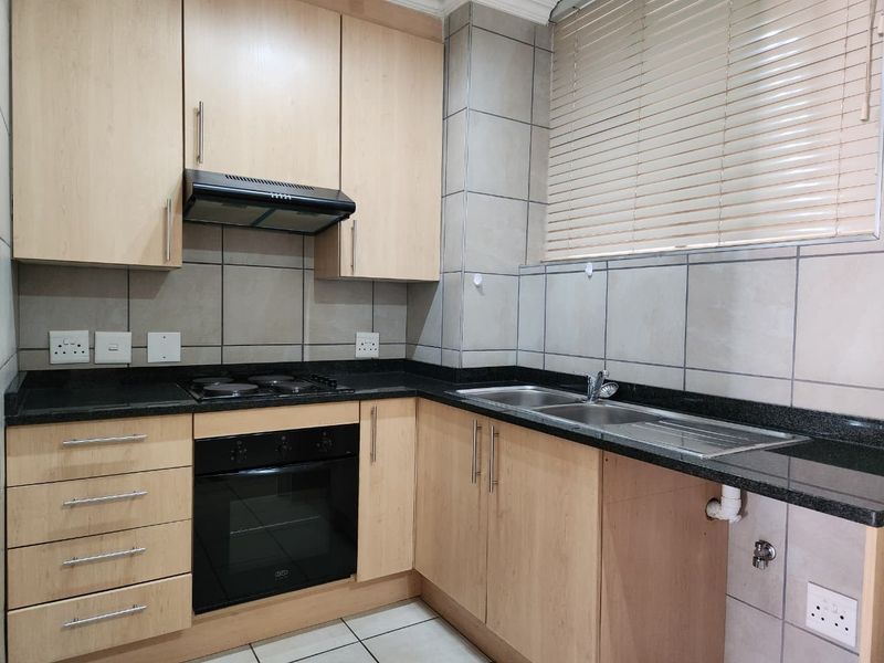 A functional kitchen featuring light wood cabinetry, granite countertops, built-in oven, electric hob, and a double bowl stainless steel sink with tiled backsplash.