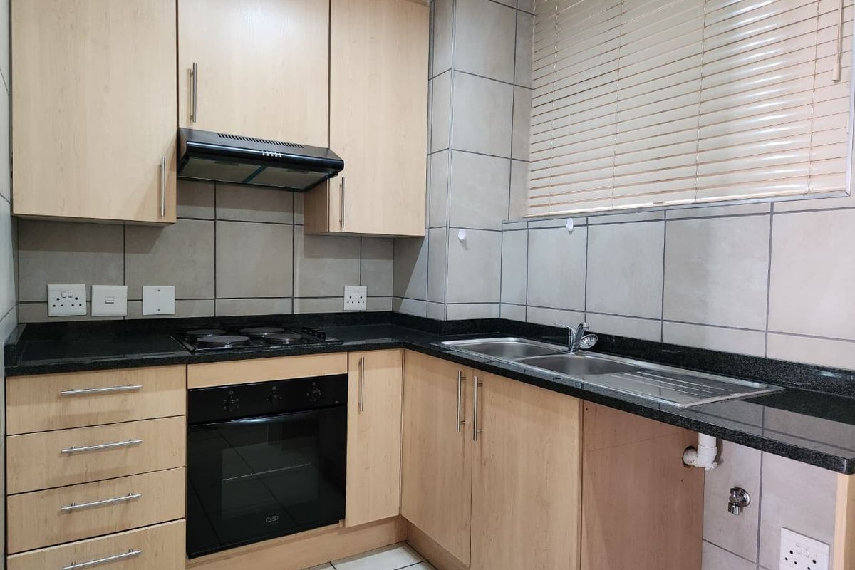 A functional kitchen featuring light wood cabinetry, granite countertops, built-in oven, electric hob, and a double bowl stainless steel sink with tiled backsplash.