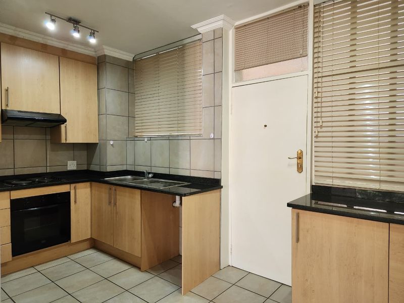 A functional kitchen featuring light wood cabinetry, granite countertops, built-in oven, hob, extractor fan, and tiled flooring with ample natural light.