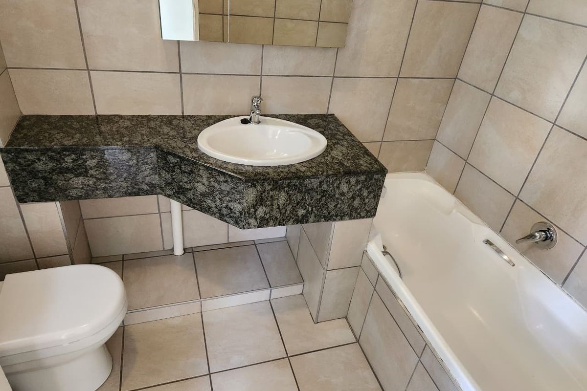 A functional bathroom featuring a granite vanity top with a basin, a bathtub, and neutral ceramic wall and floor tiling.