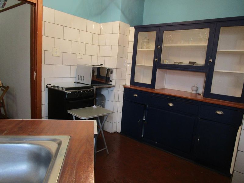 A dated kitchen featuring dark blue built-in cabinetry, a white tiled backsplash, and a stainless steel sink with a freestanding stove.