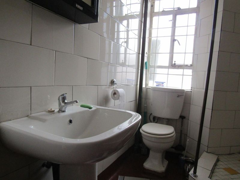 A compact bathroom featuring a pedestal basin, toilet, and tiled walls. The space requires cosmetic updates to improve its dated appearance.