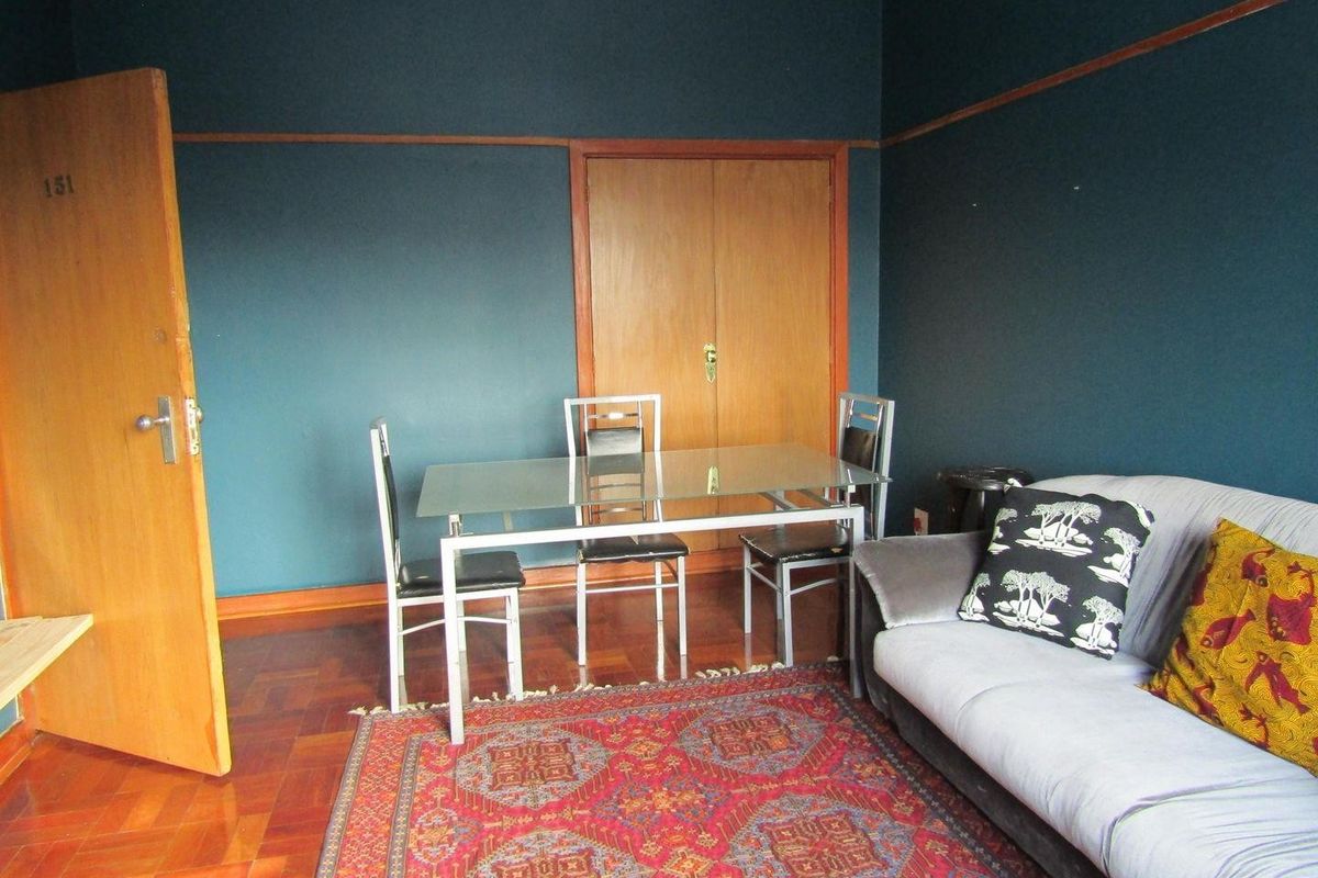 A living area featuring classic parquet flooring, dark painted walls with a picture rail, and a built-in wooden cupboard.