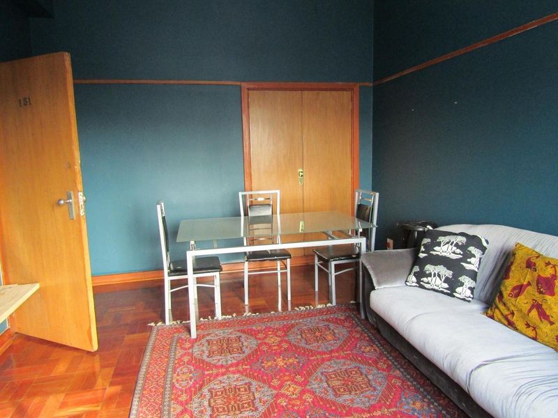 A living area featuring classic parquet flooring, dark painted walls with a picture rail, and a built-in wooden cupboard.