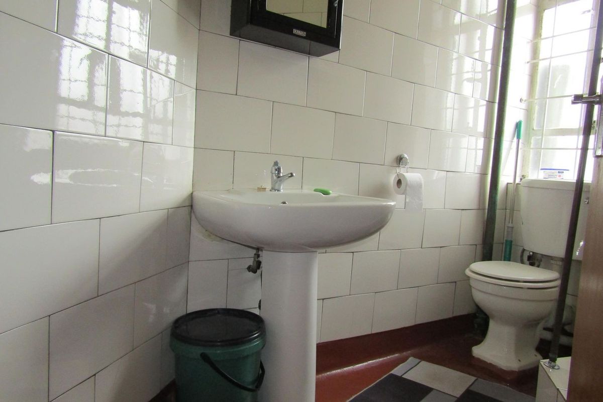 A functional bathroom featuring a pedestal washbasin, toilet, and full-height wall tiling, requiring cosmetic updates to improve its dated appearance.