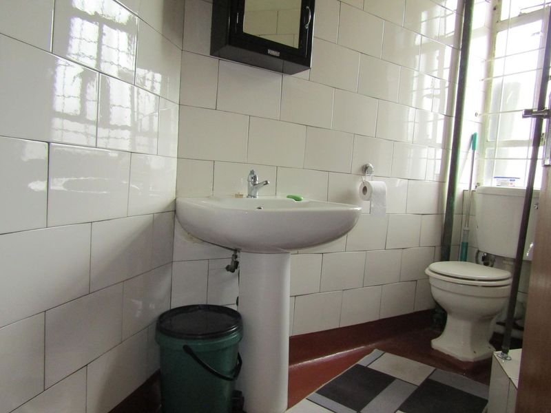 A functional bathroom featuring a pedestal washbasin, toilet, and full-height wall tiling, requiring cosmetic updates to improve its dated appearance.