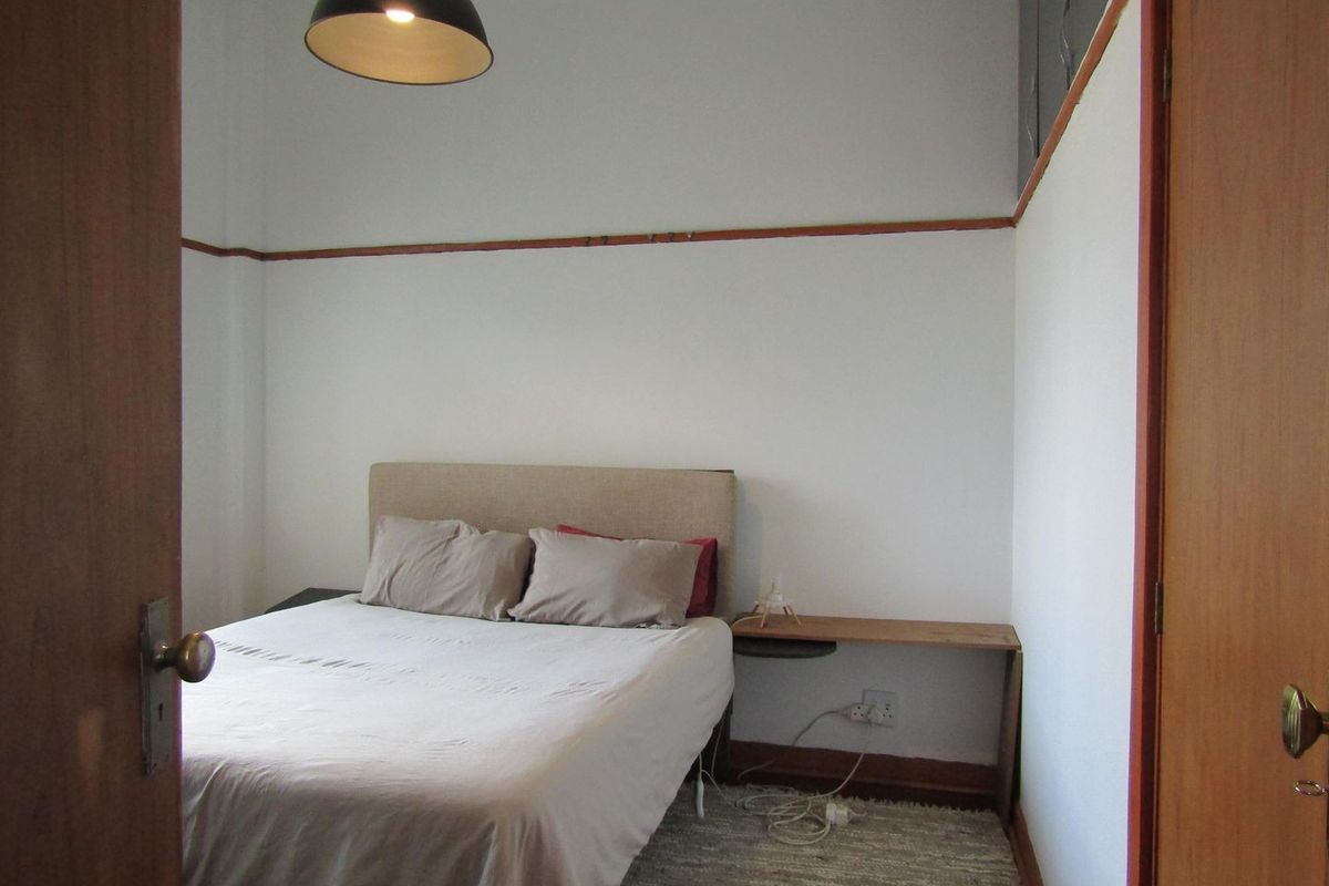 A compact bedroom featuring neutral walls, traditional picture rails, and timber door frames, offering a functional space with potential for cosmetic updates.