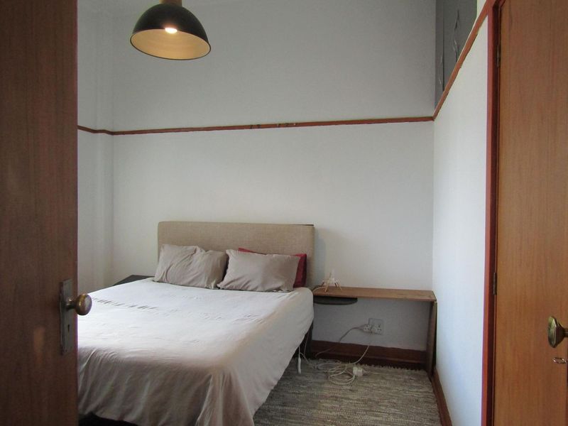 A compact bedroom featuring neutral walls, traditional picture rails, and timber door frames, offering a functional space with potential for cosmetic updates.
