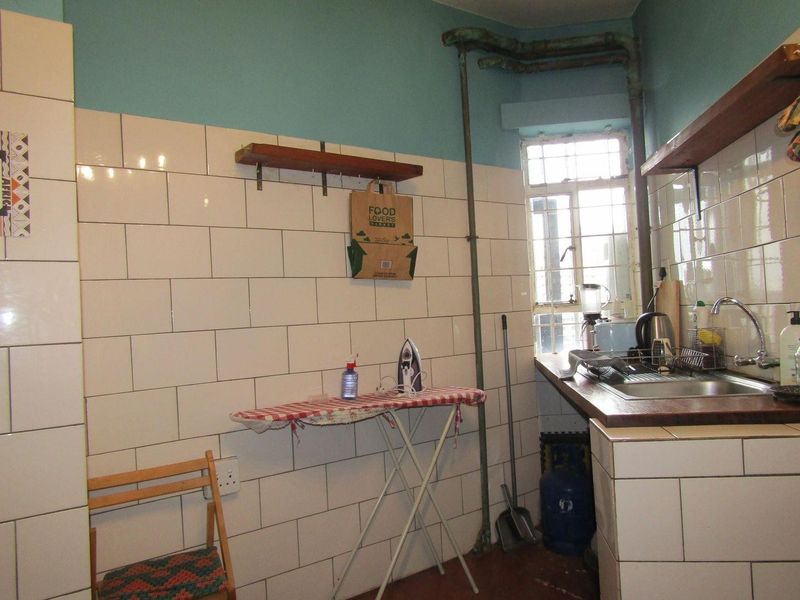 A functional scullery or utility area featuring subway tile splashbacks, a stainless steel sink, and exposed plumbing, offering potential for modernization.
